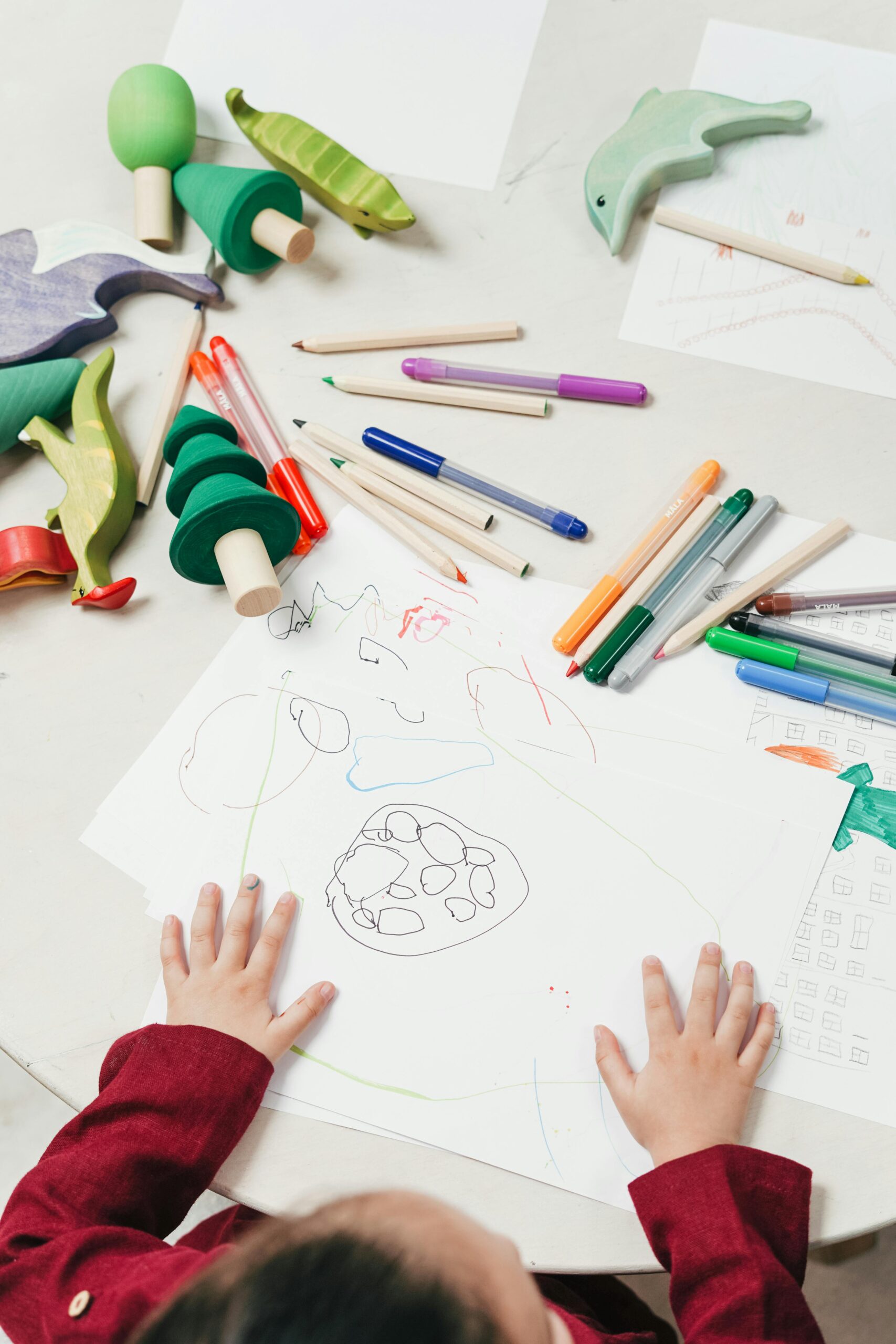 A child engages in creative drawing with colored pencils surrounded by wooden toys on a table.art-design-template