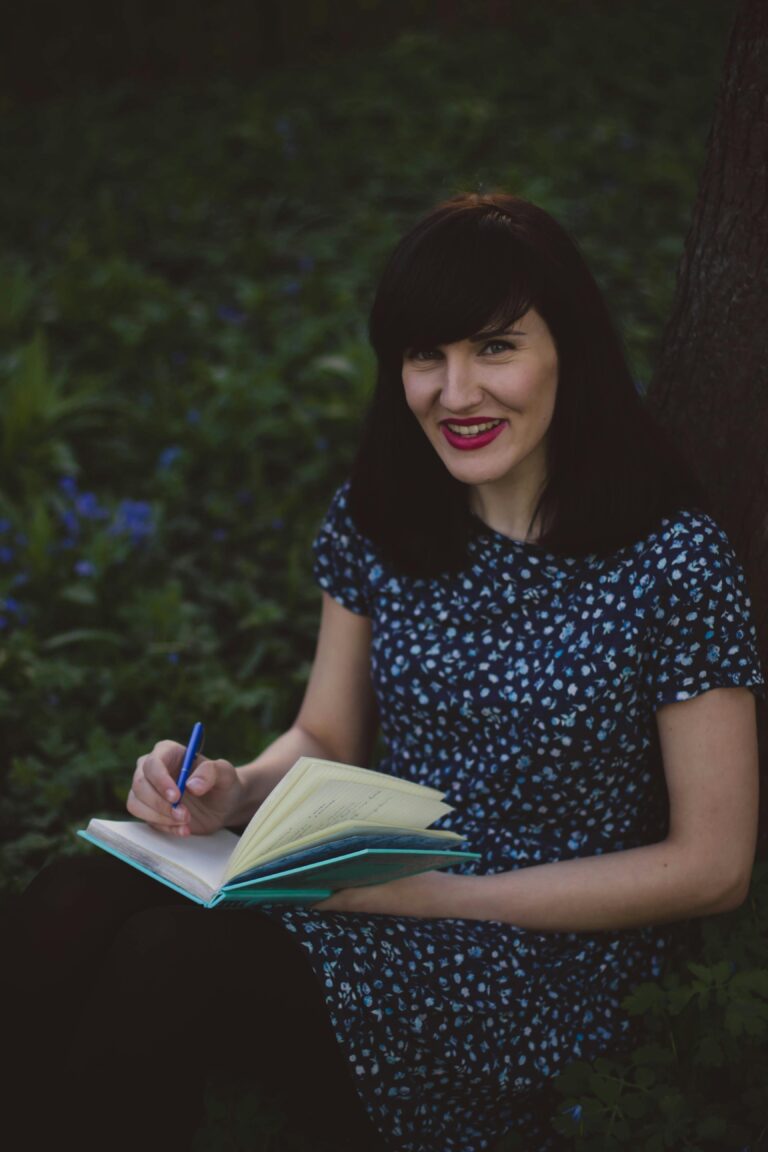 Young woman writing in a journal while sitting outdoors, enjoying nature.